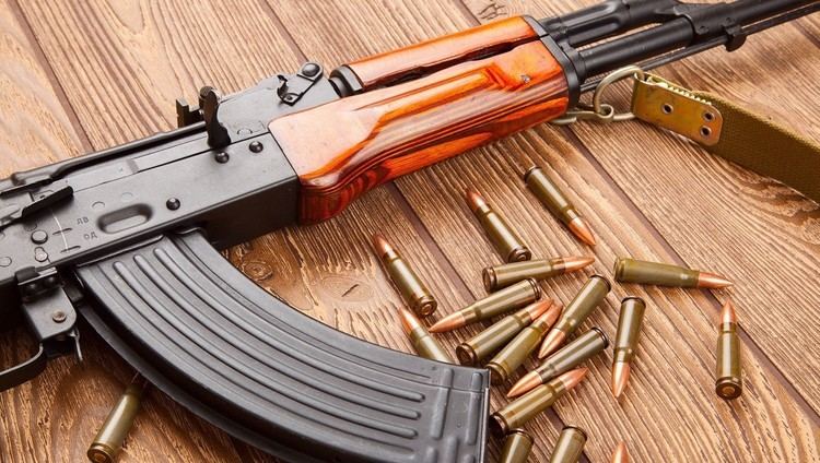 An AK-47 rifle with bullets in ammunition on a wooden floor