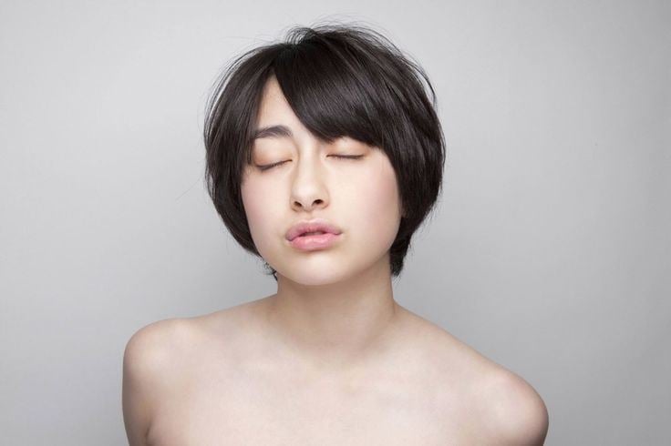 Akari Hayami is closing her eyes while pouting her lips, topless and having short black hair.