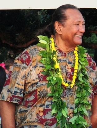 Al Harrington smiling while wearing garlands and colorful polo with a coconut tree design