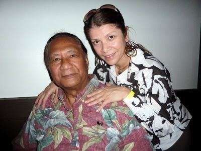 Al Harrington with a tight-lipped smile and wearing a floral polo while Rosa Harrington wearing a black and white long sleeve blouse