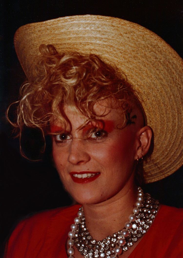 Alannah Currie smiling while wearing brown hat, necklaces and red blouse