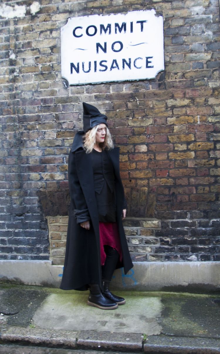 Alannah Currie looking afar while wearing black coat, black hat, black blouse and red skirt