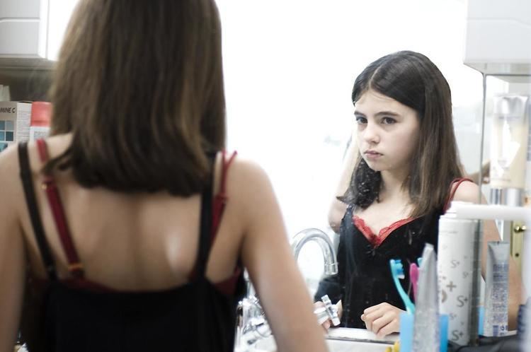 Young Alba Gaia Bellugi looking at the mirror while wearing a red brassiere and black sleeveless top