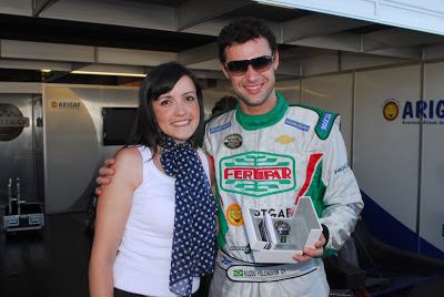 Alceu Feldmann smiling and wearing shades, white and green racing suit while the woman beside him wearing a white top and polka dot scarf