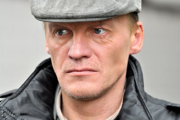Aleksei Serebryakov looking afar while wearing gray hat and black jacket