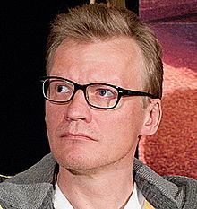 Aleksei Serebryakov wearing eyeglasses and gray jacket