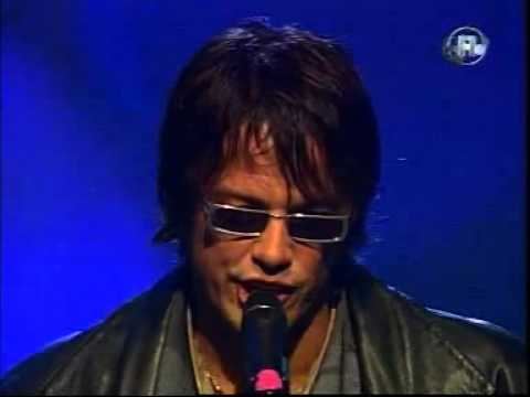 Alex Jolig singing while wearing eyeglasses, necklace, and black leather jacket