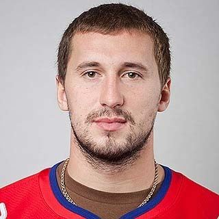 Alexander Galimov with mustache and beard while wearing a red and blue t-shirt and necklace