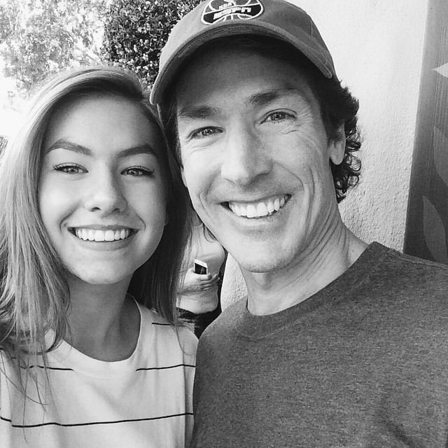 Alexandra Osteen smiling with her father, Joel Osteen and wearing a white shirt with stripes.
