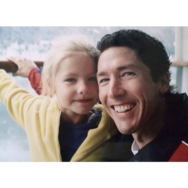 Alexandra Osteen as a child smiling with her father, Joel Osteen and wearing a purple shirt under a yellow jacket.