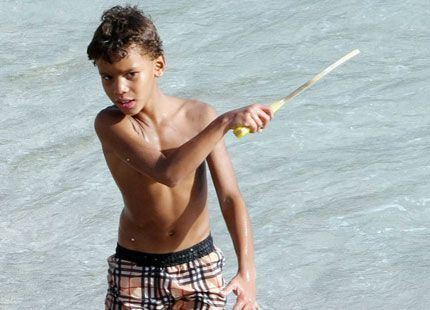 Alexandre Coste at a young age, wearing a checkered short while holding a racket at the beach.