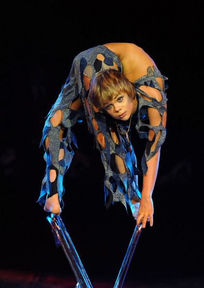Alexey Goloborodko with a serious face while doing contortion above the chair and wearing a blue contortion costume.