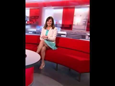 Alexis Green wearing white coat and aqua green dress while sitting on a red couch