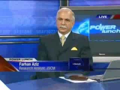 On Power Lunch, Ali Kuli Khan Khattak is serious, sits down on a black chair, has white hair and a mustache, in front is a laptop and an eyeglass case and a paper, he is wearing white long sleeves, a gold necktie under a black suit with a pocket and handkerchief on left. Below is an interview call from Farhan Aziz the Research Analyst.