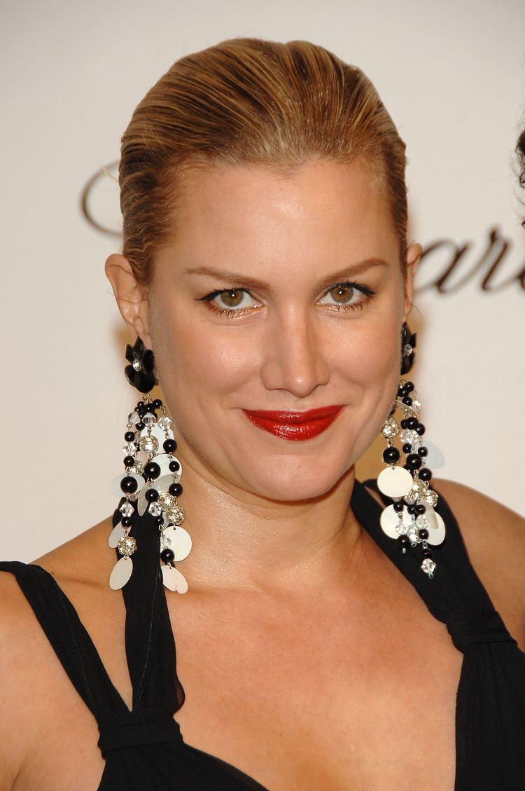 Alice Evans smiling with brown eyes, red lips, her blonde hair neatly bun, wearing beaded-dangling earrings in black and white, in a two-way black neck halter and strapped gown with a visible cleavage.