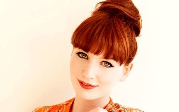 Alice Levine smiles while wearing an orange shirt