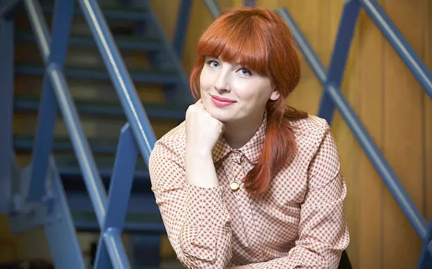 Alice Levine smiles while standing on a metal staircase