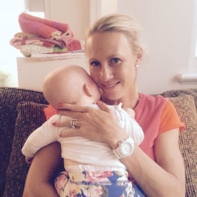 Alicia Molik smiling and holding a baby while sitting on the couch and she is wearing a pink shirt