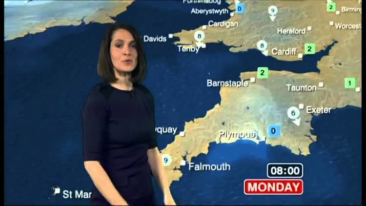 Alina Jenkins in BBC TV channel as a weather presenter, with short hair and wearing a dark blue dress.