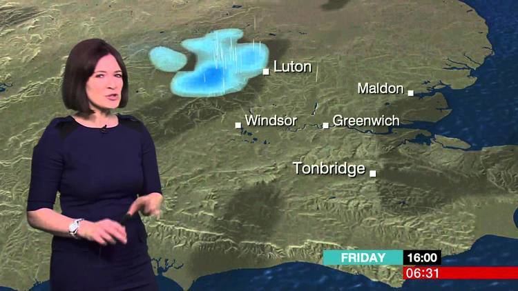Alina Jenkins in BBC TV channel as a weather presenter, with short hair, wearing a watch and a dark blue dress.