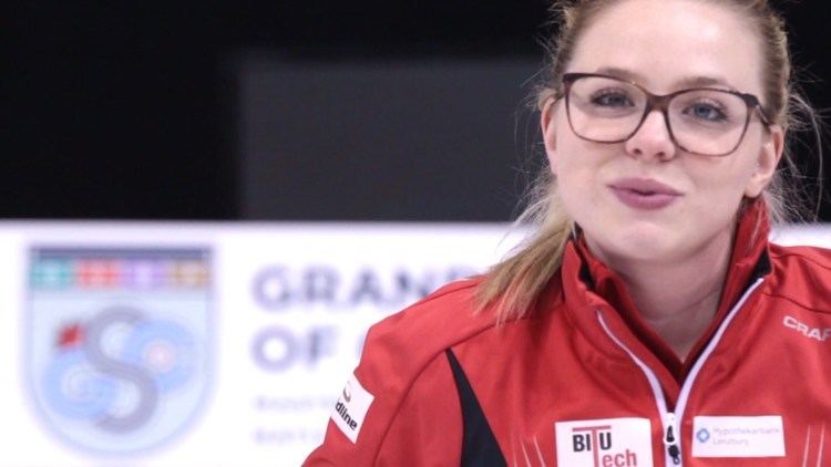 Alina Pätz smiling, with blonde hair, wearing eyeglasses and a red, white, and black jacket.