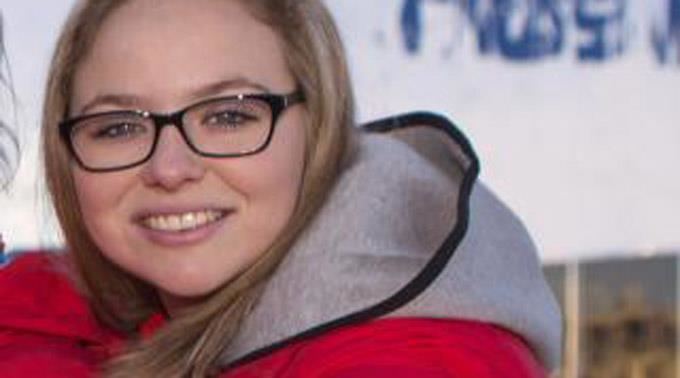 Alina Pätz smiling, with blonde hair, wearing eyeglasses and a red jacket with a gray and black hood.