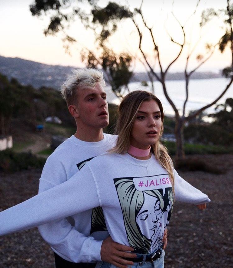 Alissa Violet and Jake Paul with a serious face while Jake holding her waist. They have both blonde hair and wearing a couple white jackets.