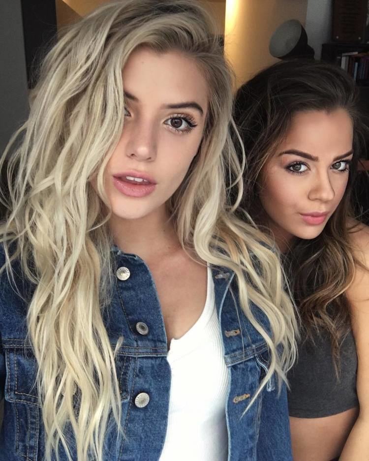 Alissa Violet with a half-open mouth and Tessa Brooks smiling. Alissa with blonde hair and wearing a denim jacket over a white shirt while Tessa with wavy hair and wearing a black crop top.