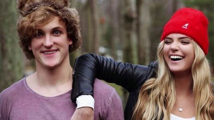 Alissa Violet and Logan Paul are smiling. Alissa with blonde hair, wearing a red bonnet, a black jacket over a white shirt while Logan wearing a purple shirt.
