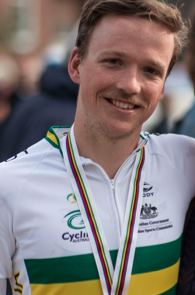 Alistair Donohoe smiling while wearing a white, green, and yellow jersey and medallion