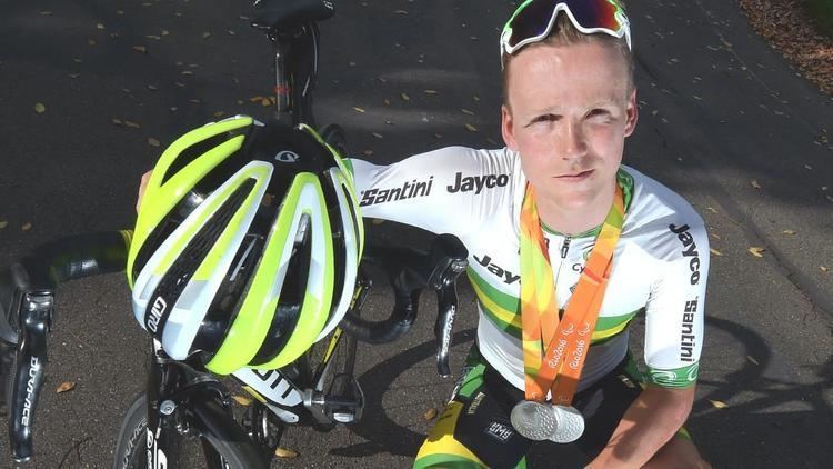 Alistair Donohoe with a tight-lipped smile while sitting beside his bike and wearing a white and green jersey and his medal for the Rio Games