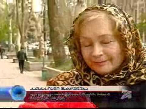 Alla Dudayeva features on the news while closing her eyes, with blonde hair, wearing a black and yellow headscarf and black dress.