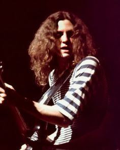 Allen Collins playing a guitar on stage while wearing a striped black and white shirt.