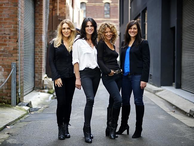 Ally Fowler smiling with her friends while wearing a black blazer, blue inner top, jeans, and black boots