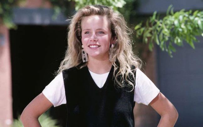 Amanda Peterson smiling, with curly blonde hair, and wearing a white and black shirt.
