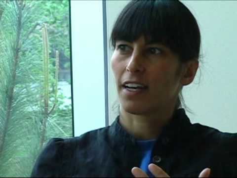 Amy Balkin talking in an interview about Systems of Sustainability wearing a black jacket and a blue shirt.