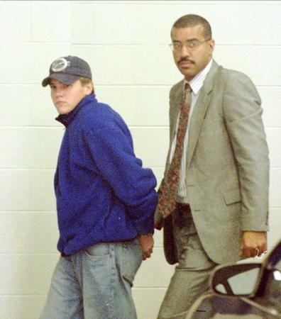 Brian Peterson wearing a cap and blue sweatshirt while his lawyer is wearing a beige coat, pants, long sleeves, and necktie
