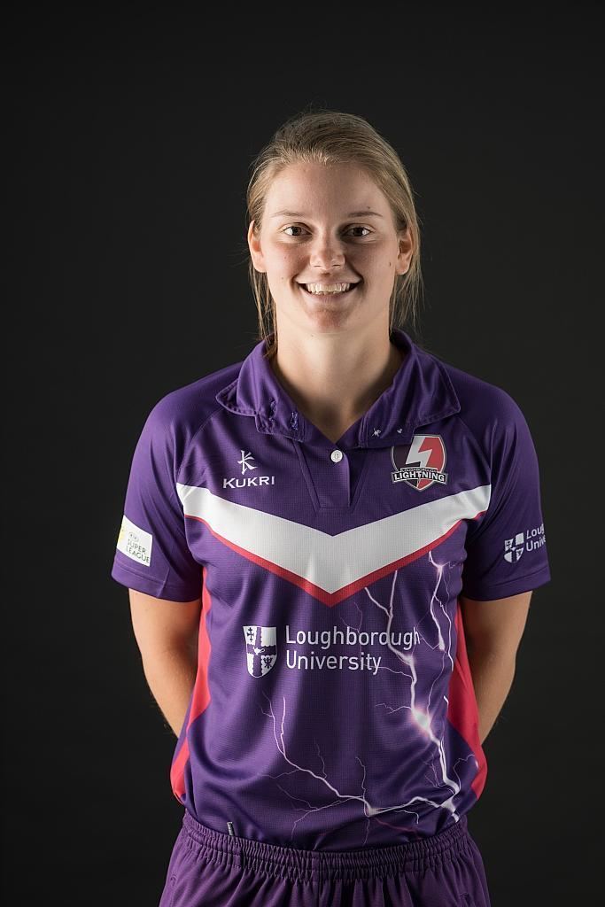 Amy Jones smiling while wearing a violet, white and red polo shirt