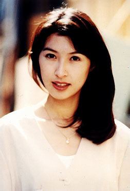 Amy Kwok smiling while wearing a white blouse and earrings