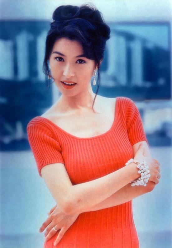 Amy Kwok smiling while her arms crossed and she is wearing an orange knitted dress, earrings, and bracelet