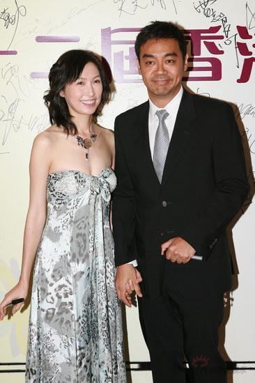 Amy Kwok and Sean Lau are smiling and Amy is wearing a gray and white tube dress while Sean is wearing white long sleeves, a black coat, and gray necktie