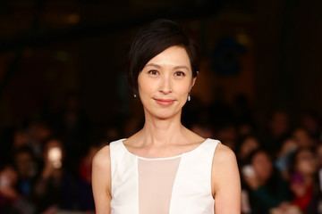 Amy Kwok with a tight-lipped smile while wearing a white sleeveless blouse and earrings