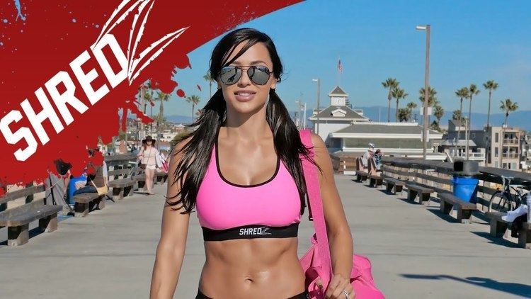 Ana Cheri smiling with a two ponytail hairstyle and wearing a pink sports bra, sunglasses while carrying a pink bag