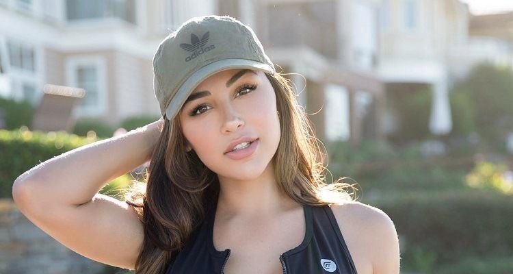 Ana Cheri looking fierce with her hand at the back of her head and hair down while wearing a sexy black sports bra and gray cap