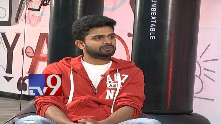 Ananda Vardhan with mustache and beard while wearing a red and white jacket, white t-shirt, and denim pants