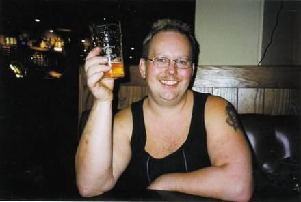 Anders Eklund wearing a black sando, holding a glass of beer with a tattoo on his arm.