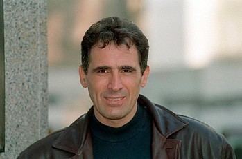 Andrew Kazamia smiling while wearing a brown leather jacket and a black shirt.