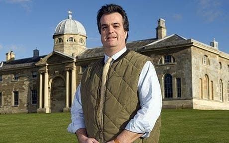 Andrew Russell, 15th Duke of Bedford, smiling while wearing a moss green gilet, white long sleeves, and necktie