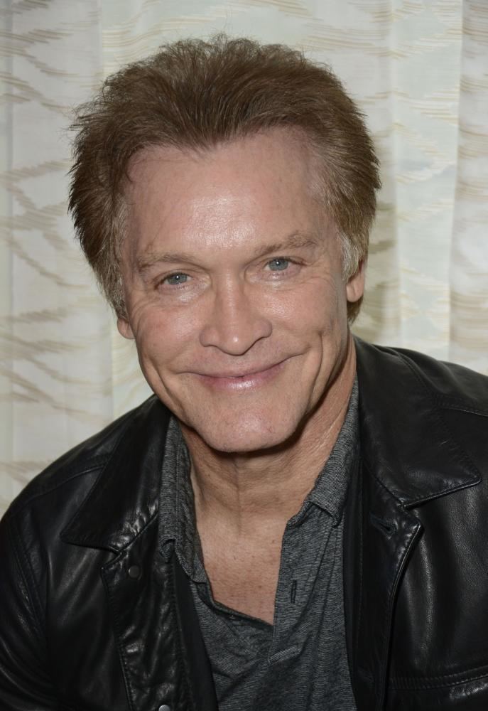 Andrew Stevens with a tight-lipped smile while wearing a black t-shirt and black leather jacket