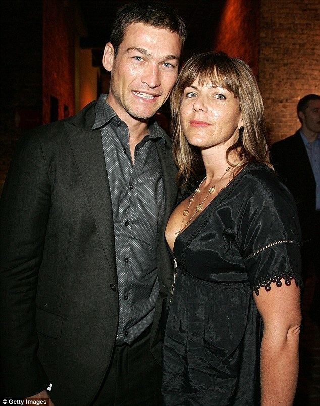 Andy Whitfield smiling with his wife Vashti Whitfield while wearing a black suit, black pants, and dark gray long sleeves.